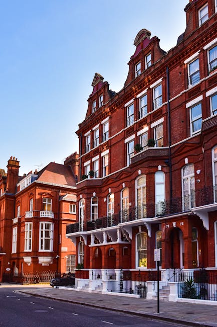 A wide view of a historic residential building with a cream-colored facade, multiple rows of large sash windows, and decorative architectural details, situated on a London street under a partly cloudy