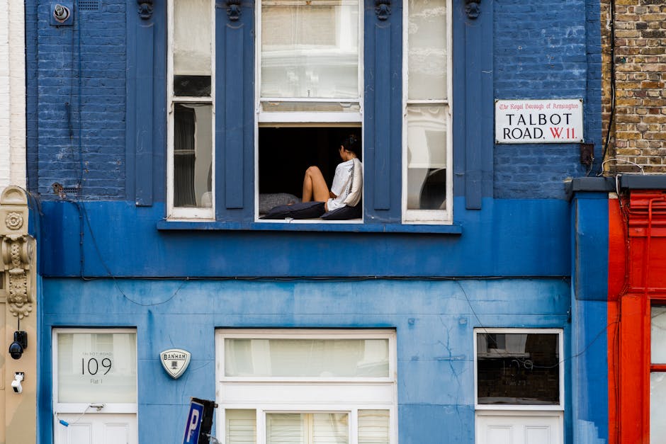 The image depicts the exterior of a shopfront located on a quiet street in West Kensington, featuring a pastel green facade with large glass windows displaying various plants and flowers inside. The s